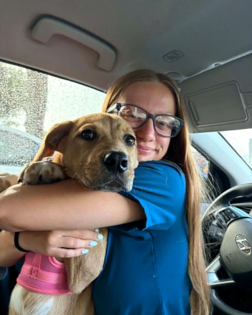 Isabella hugging a happy tan puppy in a pink harness