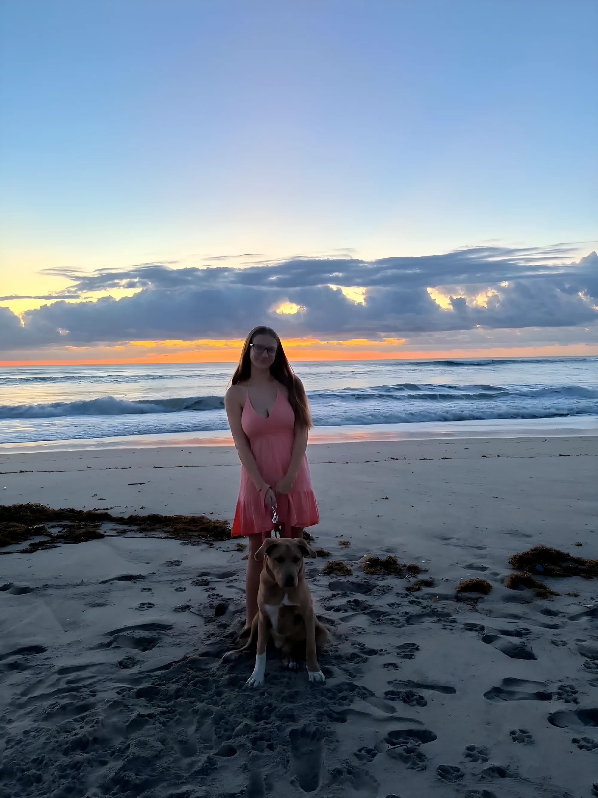 Isabella on the beach at sunrise with her dog sitting at her feet